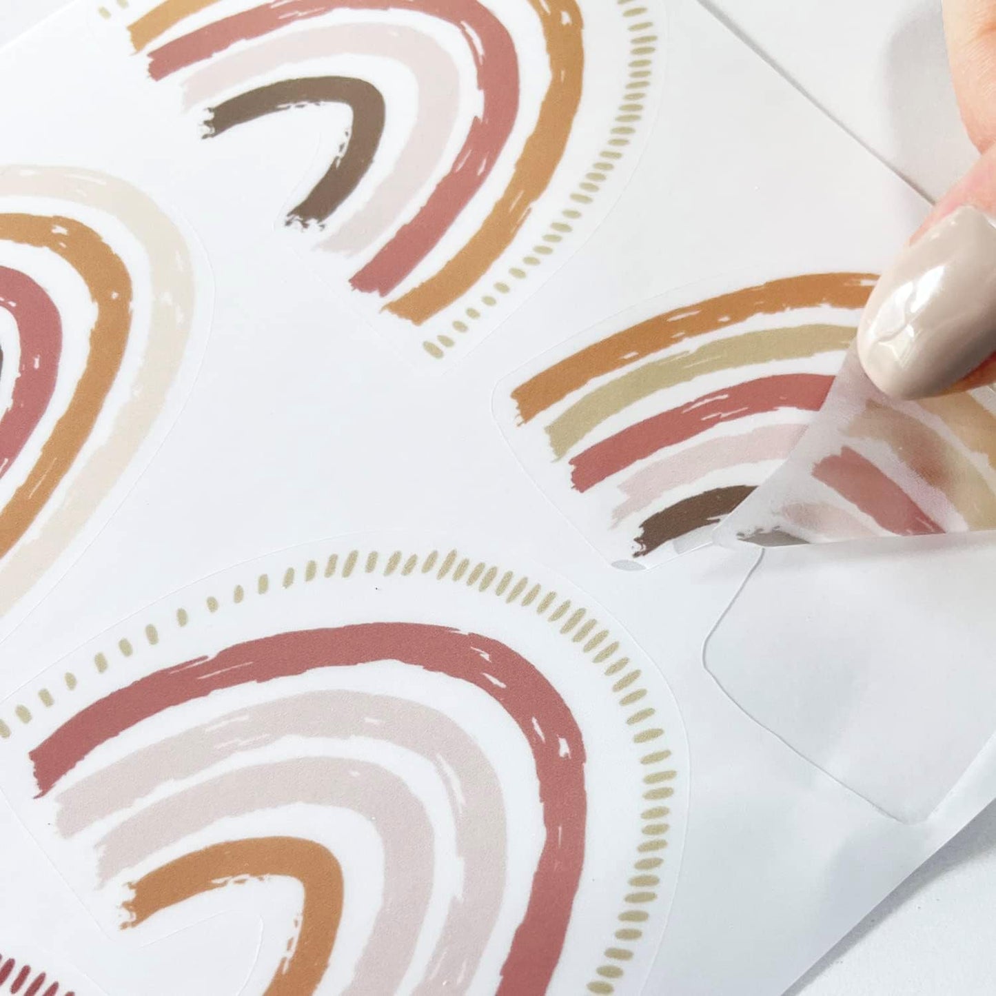 DreamyWalls muurstickers regenboog kinderkamer in zachte pastelkleuren met hand die sticker losmaakt